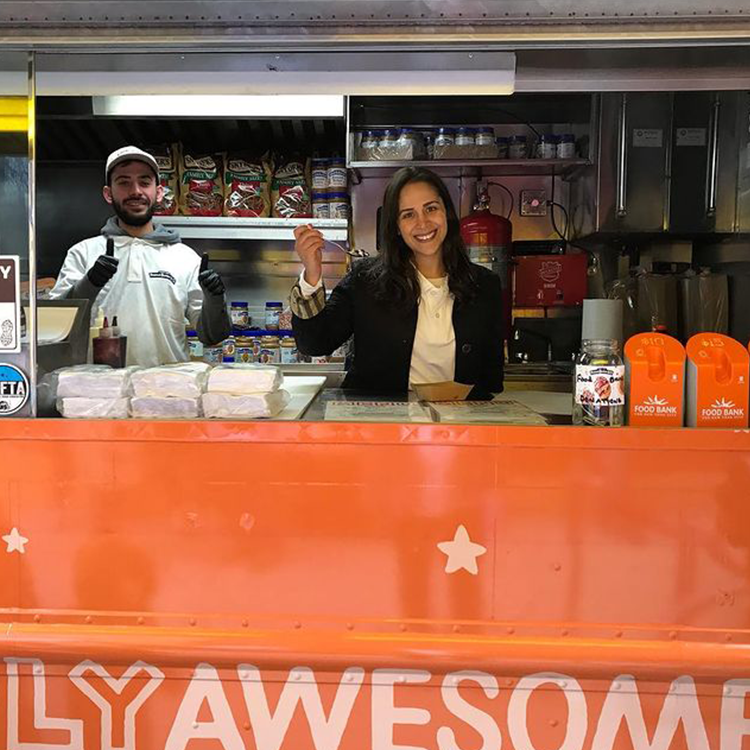 Two people smiling inside an orange food truck.